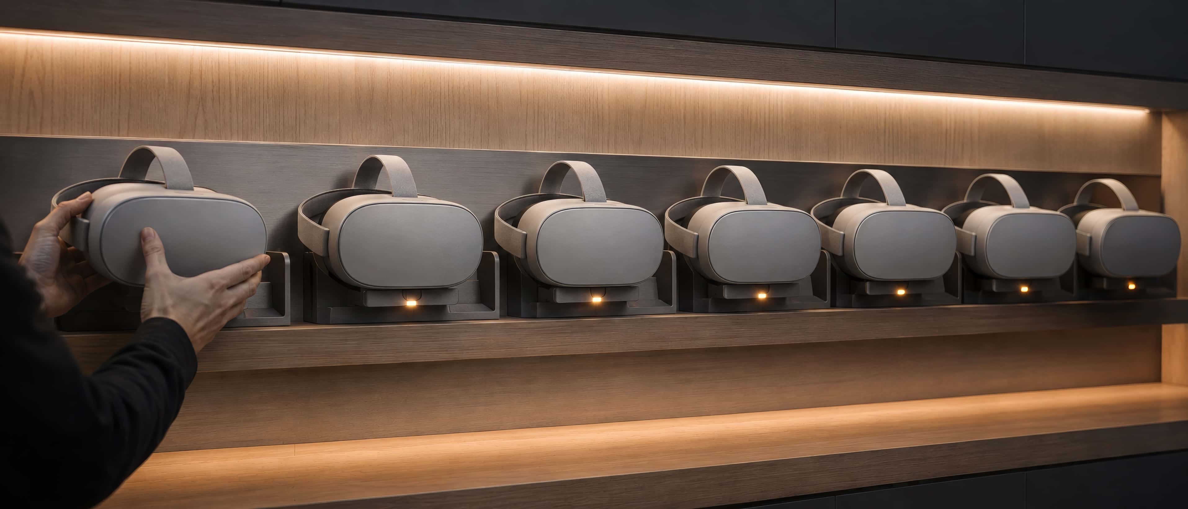 A tidy wall charging station where six identical unbranded headsets wait, discreet status lights on, in an impeccable equipment room.